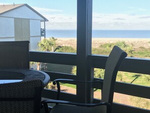 A balcony with a view of the ocean, a small table, and a chair.