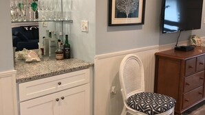 Quarto com cozinha, uma cadeira de jantar, televisão e uma obra de arte emoldurada na parede.