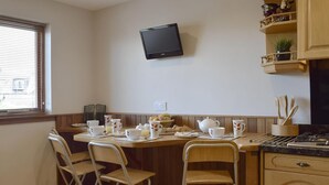 A kitchen with a dining table set for four, a TV mounted on the wall, and wooden cabinets. - 2 bedroom accommodation in Auchterarder (Auchterarder)