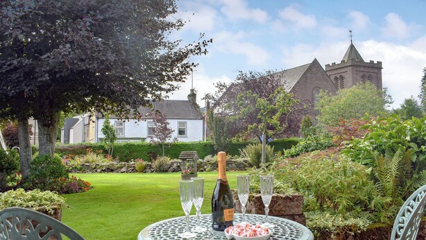 A garden patio with a table set for two, a bottle of champagne, and a plate of shrimp. - 2 bedroom accommodation in Auchterarder (Auchterarder)