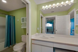 Une salle de bain avec un lavabo blanc, un miroir avec éclairage intégré, des toilettes et un rideau de douche.