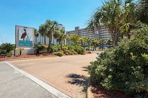 Un chemin piétonnier pavé mène à un bâtiment sur lequel on peut lire l’inscription « Navarre Beach Regency ».