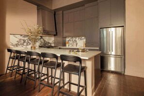 A modern kitchen with a central island, bar stools, stainless steel appliances, and marble backsplash.