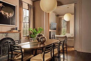 A dining area with a round table, chairs, and a fireplace. There is a television on a stand and a plant in the corner.