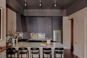 Uma cozinha moderna com armários escuros, bancada de mármore, geladeira de aço inoxidável e um espaço de bar com quatro banquetas.