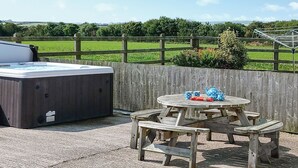 An outdoor patio with a hot tub and a wooden table with chairs.