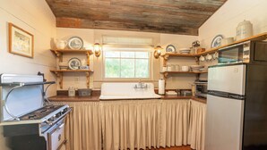 Una cocina con armarios de madera, estufa, refrigerador y una ventana con cortinas.