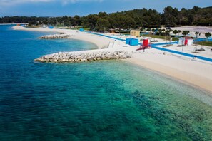 A coastal beach with clear turquoise waters, a sandy shore, and a small building with a red roof.