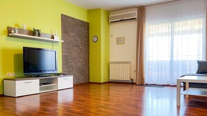 Una sala de estar moderna con televisor de pantalla plana, piso de madera, aire acondicionado instalado y un ventanal con cortinas traslúcidas.