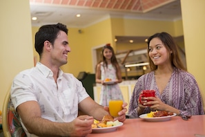 Un coin repas avec une table dressée pour deux personnes, une assiette de nourriture et une tasse rouge.