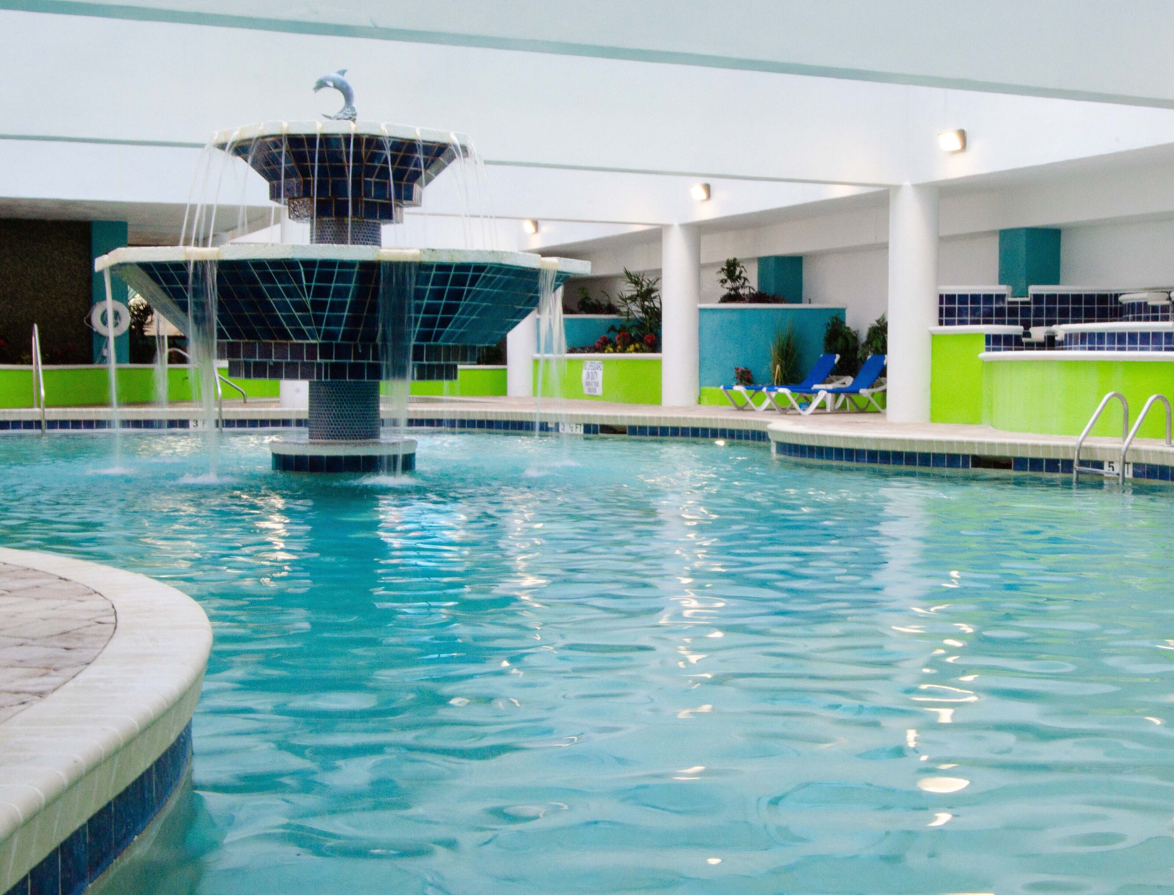 A swimming pool with a central fountain, surrounded by lounge chairs and a tiled deck.