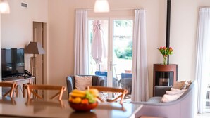 A modern living room with a sofa, a dining area with chairs, a TV, and a small table with fruit.