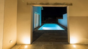 A swimming pool area with a wooden deck and a night-time view.