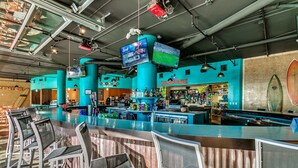 Un espace bar doté de plusieurs écrans, d’un comptoir et de tabourets de bar.