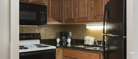 A kitchen with wooden cabinets, a black refrigerator, a white stove, and a microwave.