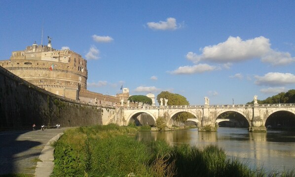 A historic stone bridge with arches over a river, leading to a large fortress-like building with multiple levels and a statue on top. - Oasis in ROME NORTH (Roma)