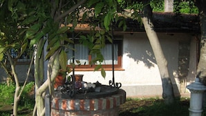 A traditional stone well with a metal spout, surrounded by greenery and a building with a tiled roof in the background. - Oasis in ROME NORTH (Roma)