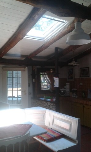 Cozy interior with high ceiling, exposed beams, and a skylight. Features a seating area, kitchen with cabinets, and a door to the outside.