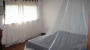 A bedroom with a bed covered by a mosquito net, a window with white curtains, and a wooden ceiling. - Oasis in ROME NORTH (Roma)