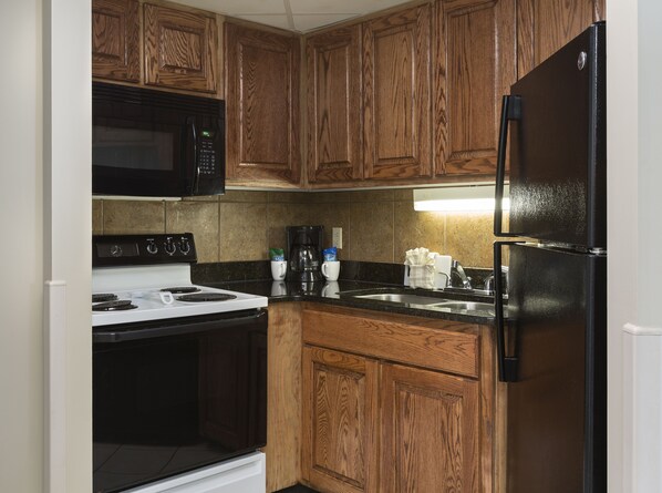 A kitchen with wooden cabinets, a black refrigerator, a white stove, and a microwave. - Deluxe Executive Suite w/ Angle Ocean View + Official On-Site Rental Privileges (Myrtle Beach)
