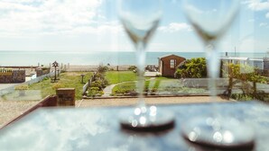 Vista attraverso una vetrina con due bicchieri di vino, su una spiaggia, una struttura in legno e una zona erbosa.