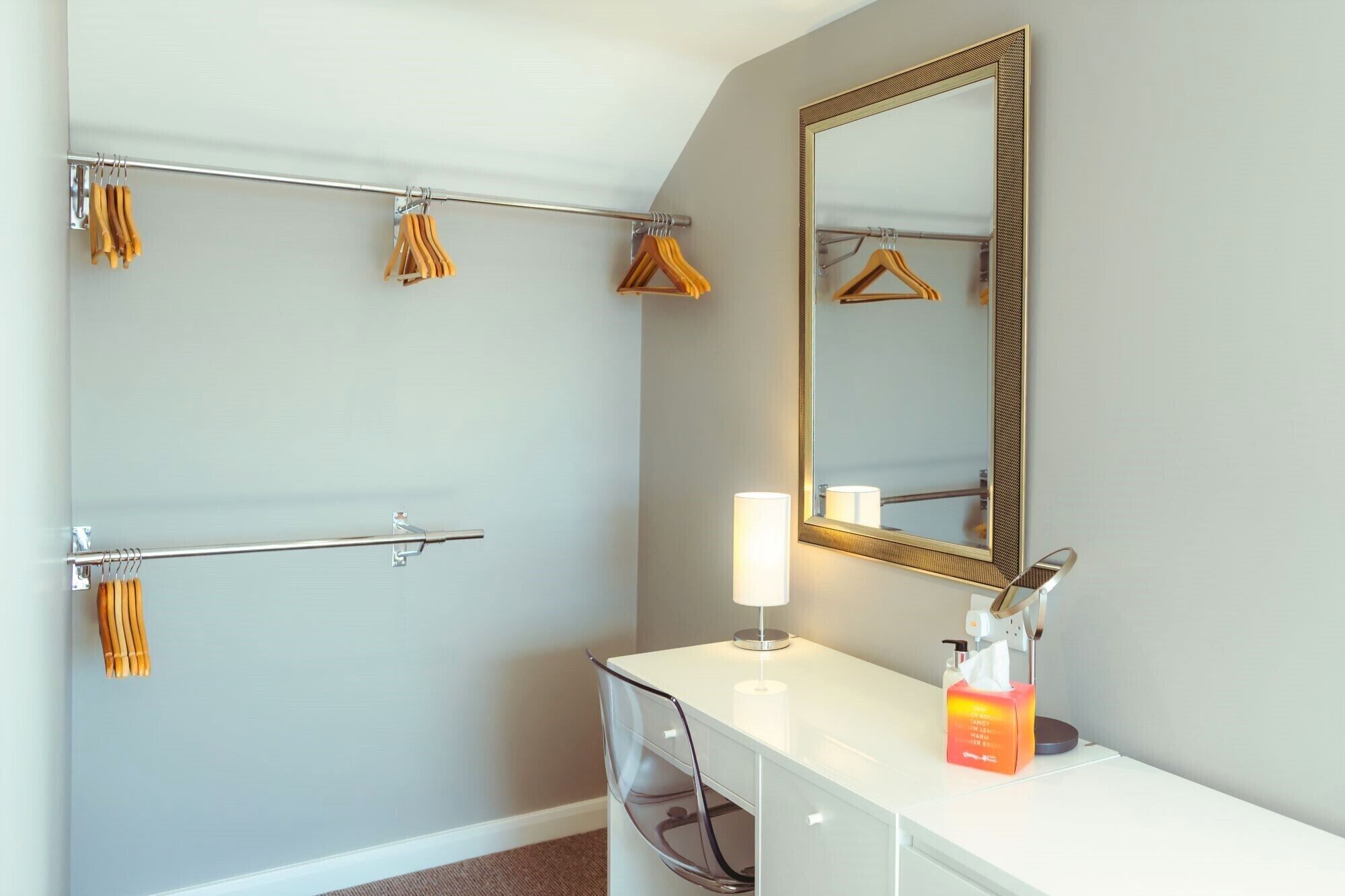 Une salle de bain équipée d’un porte-serviettes, d’un miroir, d’une commode avec une lampe et d’une boîte à mouchoirs.