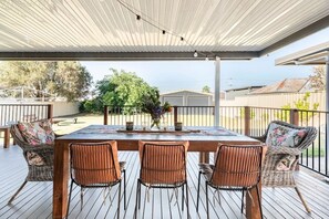 A covered outdoor patio with a wooden table and wicker chairs, overlooking a residential area.