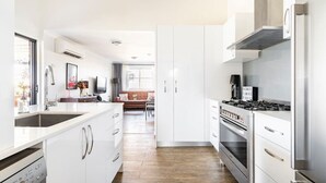 Une cuisine moderne avec des meubles blancs, des appareils électroménagers en acier inoxydable et un plancher en bois.