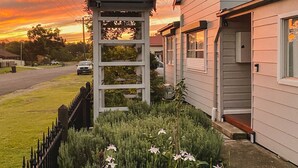 Une maison d’habitation avec un porche, un jardin fleuri et un coucher de soleil en arrière-plan.