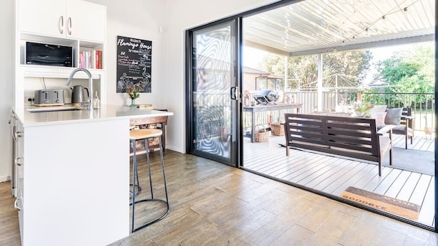 Une cuisine moderne dotée d’un îlot central intégré, d’un coin repas avec un banc et d’une porte-fenêtre coulissante donnant sur une terrasse extérieure.