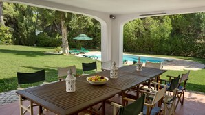 Eine überdachte Terrasse mit Pool, Gartenmöbeln und Blick auf den umliegenden Garten.