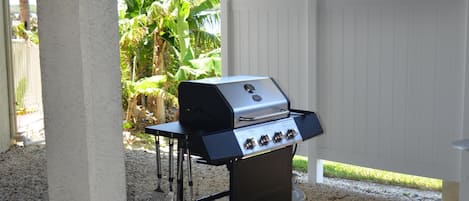 Een terras buiten met een barbecue, een tafel en een witte omheining.