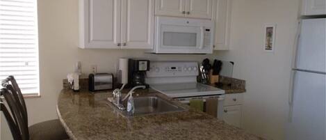 A kitchen with white cabinets, a granite countertop, a microwave, a stove, and a refrigerator.