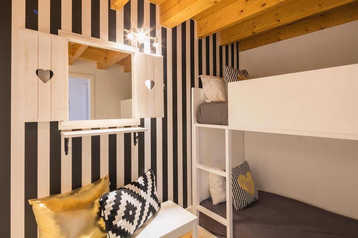 A bunk bed room with a mirror above the lower bunk, striped walls, and a wooden ceiling.