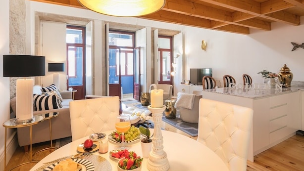 A modern living room with a dining area, featuring a round table with a white tablecloth, a chandelier, and a sofa with striped cushions. - Oporto Golden Apartment - your luxury choice in the Heart of Porto (Porto)