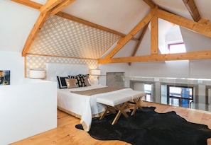 A bedroom with a bed, bedside tables, a bench, a patterned ceiling, and a view through a window.
