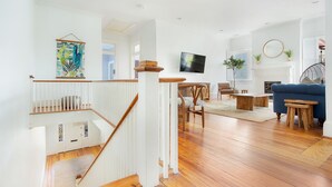 A spacious living room with a wooden staircase, a blue sofa, a fireplace, and a television mounted on the wall.