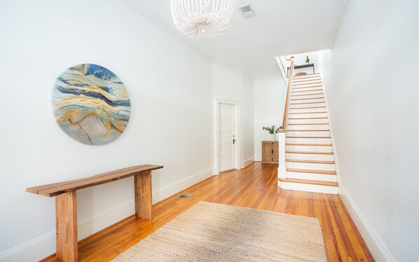Un pasillo con un banco de madera, una obra de arte circular, una escalera y una puerta.