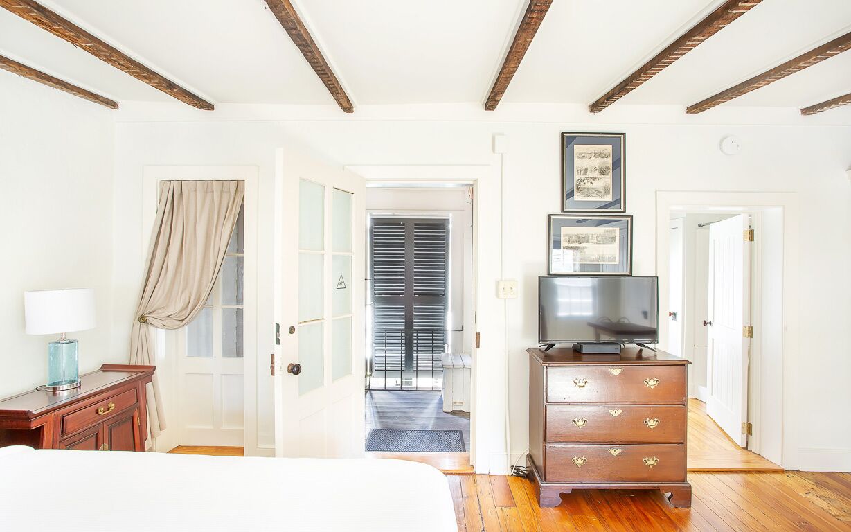 Une chambre d’hôtel avec un lit, une commode en bois, une télévision et un couloir menant à une porte.