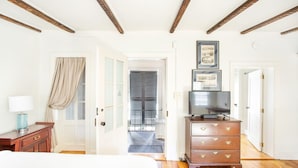 A hotel room with a bed, wooden dresser, TV, and a hallway leading to a door.