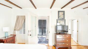A hotel room with a bed, wooden dresser, TV, and a hallway leading to a door.