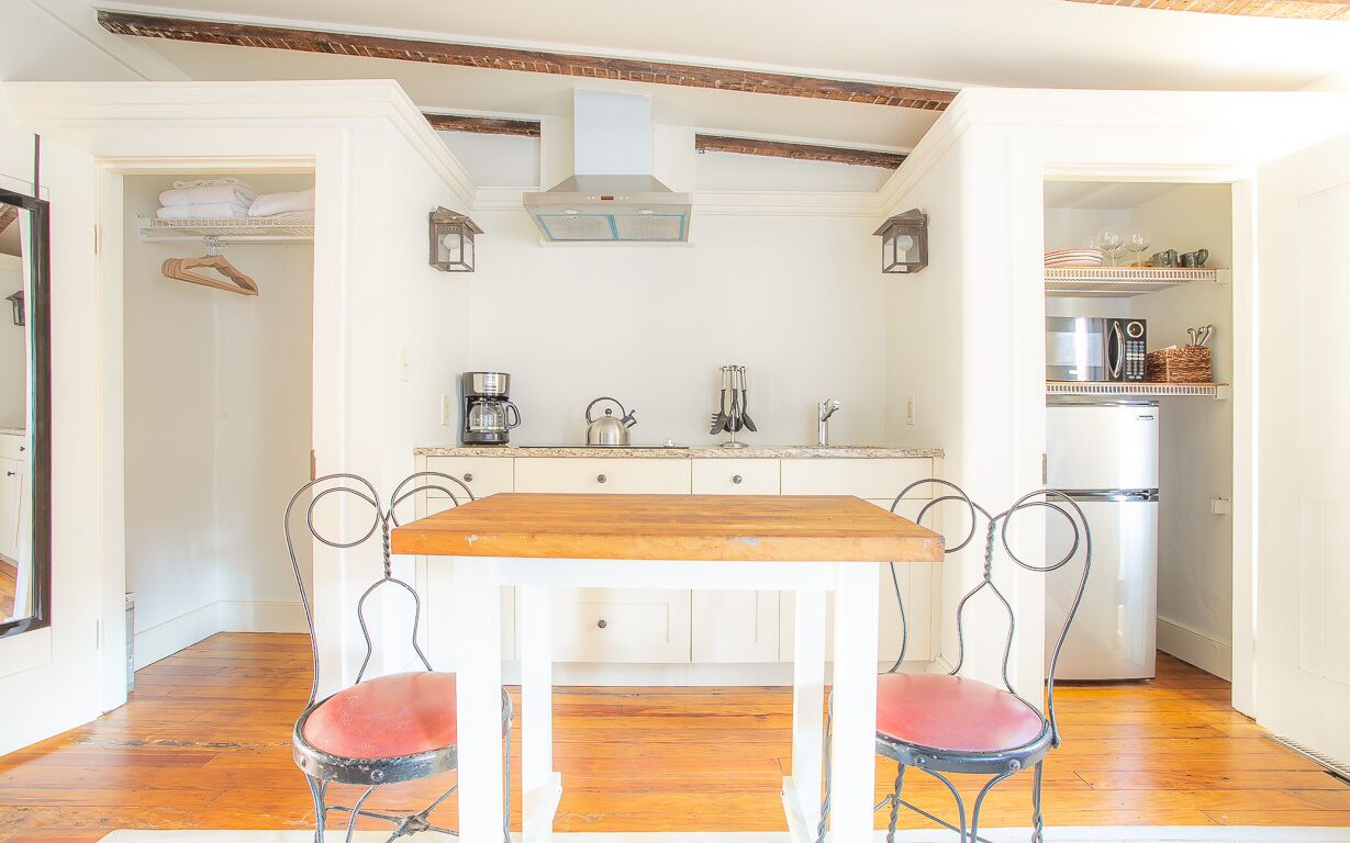 Een keuken met een houten tafel, twee stoelen, een koffiezetapparaat en een koelkast.