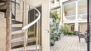 A spiral staircase leading to a second-floor balcony with outdoor seating and potted plants.
