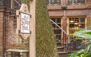 Une pancarte en bois portant l’inscription « The Wilkes House », fixée à un arbre devant un bâtiment en briques doté de fenêtres et d’un escalier.