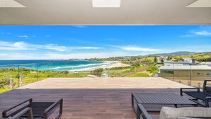 A spacious balcony with a wooden floor and two chairs, overlooking a beach and coastal town. - Seascape, Bombo, South Coast (Bombo)
