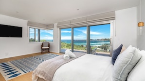 A modern bedroom with a large bed, a TV mounted on the wall, and a view of the sea through large windows. - Seascape, Bombo, South Coast (Bombo)