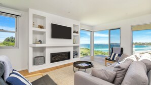 A modern living room with a fireplace, a flat-screen TV, and a large window offering a view of the ocean. - Seascape, Bombo, South Coast (Bombo)