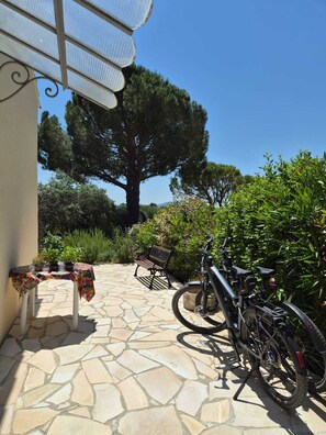 A patio with a stone floor, a bicycle, a bench, and a table with a colorful tablecloth.
