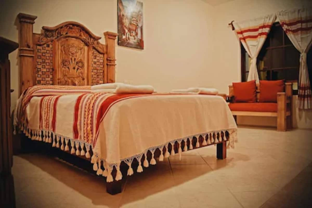 A bedroom with a wooden headboard, a bed with a white and red striped bedspread, and a wooden bench with red cushions.