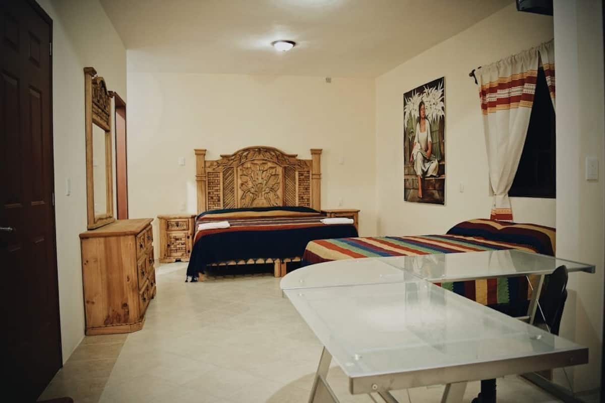 A bedroom with a wooden headboard, a bed with a colorful blanket, a wooden dresser, and a glass table.
